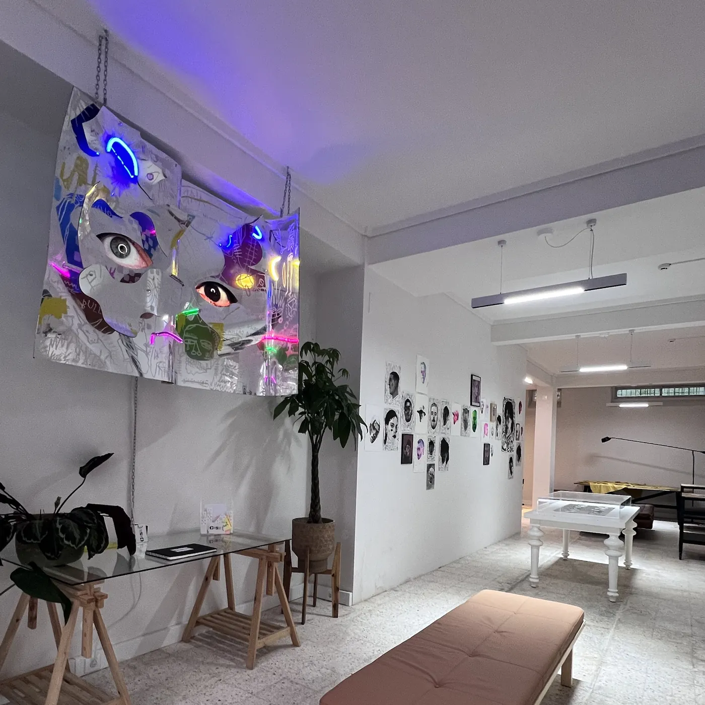 Interior da Casa Compósito: escultura de néon suspensa, banco, parede de retratos e vitrine