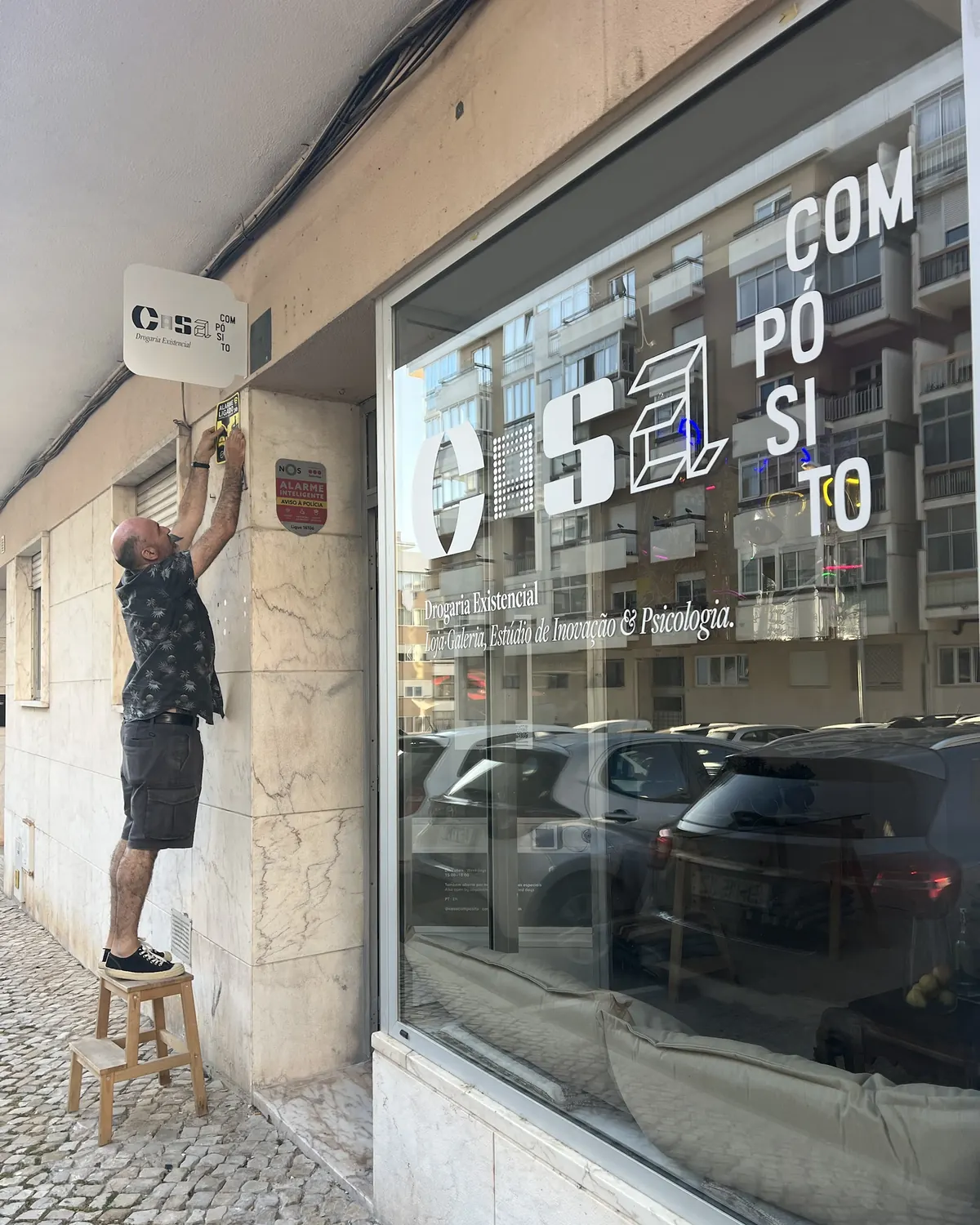 João Soares em cima de um banco a pôr o letreiro da Casa Compósito na fachada